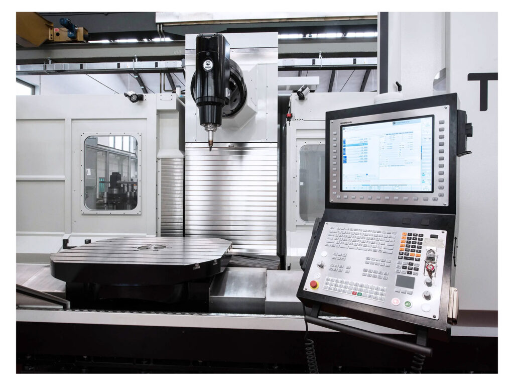 Close-up view of the Gruppo Parpas THS100 sold by Leader CNC Technologies. The machine features a large worktable with a precision tool mounted on a spindle for milling or machining operations. A digital control panel is prominently displayed on the right, used to input commands and monitor the machining process. The machine's surrounding environment is clean, with well-lit spaces typical of industrial workshops. The overall setup is designed for high-precision, automated manufacturing tasks.