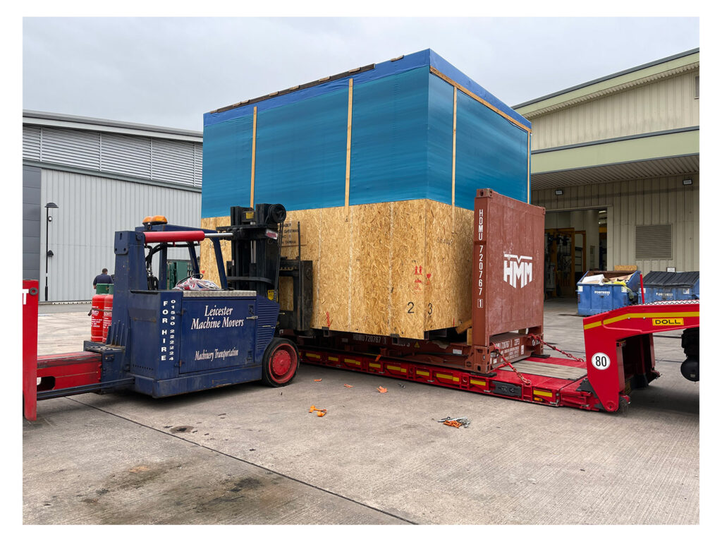 Heavy duty forklift lifting a box with a CNC machine in it. The machine/box is being lifted from the back of a flatbed lorry.